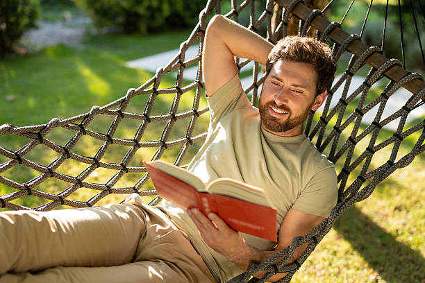 istock Caucasian bearded young man lying in hammock with a book in hands 2239108282