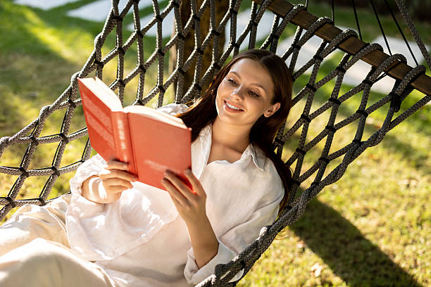 istock Long-haired caucasian young woman enjoying leisure while lying in hammock with a book 2239108287