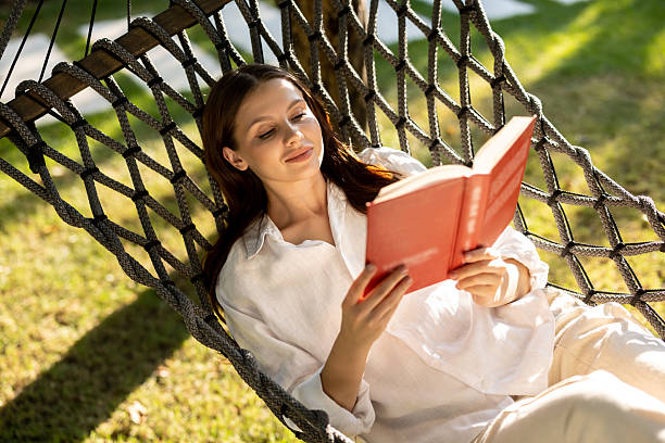 istock Young woman lying in hammock, reading a book and looking contented 2239108291