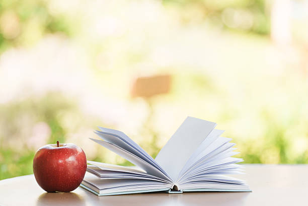 An open book laid beside a fresh apple on a wooden table with a softly blurred background evoking a cozy and peaceful atmosphere.