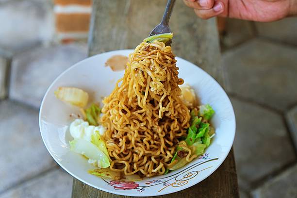 Close-up of hand lifting cooked instant noodle with fork. Asian comfort food concept showing texture and appetite appeal.