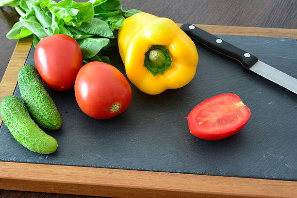 Fresh wet red and yellow tomatoes with peppers, garlic and a knife on a table