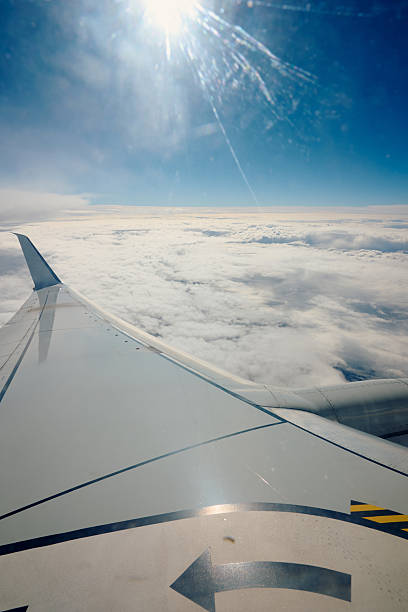 istock Airplane wing flying above clouds with sun 2239120982