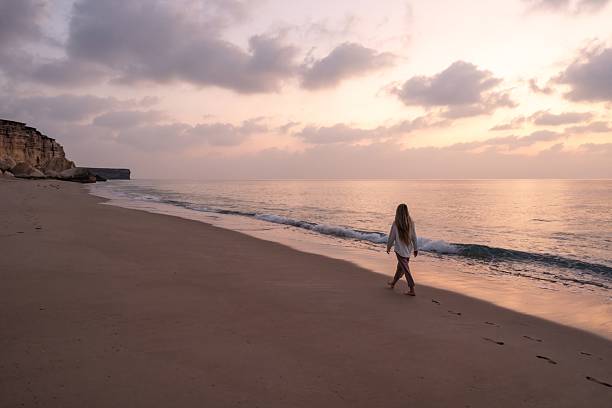 istock Woman walking alone on beach at sunset in oman 2239133428