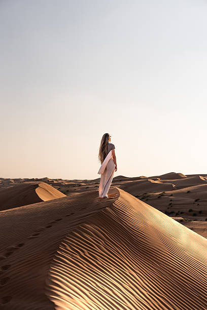 istock Woman standing on desert dune looking at sunset landscape 2239133486
