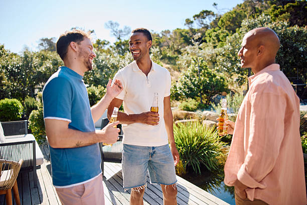 istock Three cheerful young men chatting with drinks in hand outdoors at sunny vacation property with an idyllic natural landscape 2239142414
