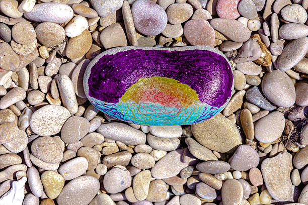 Stone illustrated with sea, sun and sky by child using felt tip pens surrounded by pebbles