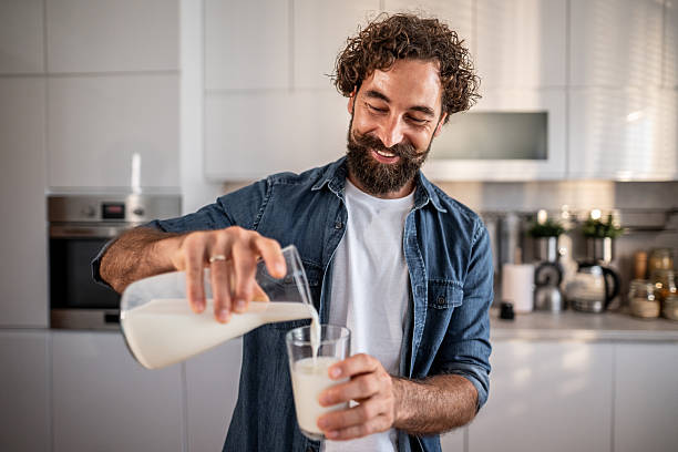 istock Happy man pouring milk into glass in kitchen 2239144987