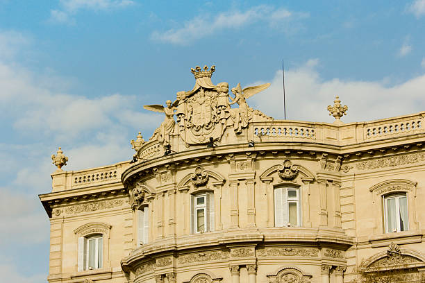 Madrid, Spain - January 18, 2010: Ornate architectural facade of a historic building in Madrid, Spain, showcasing intricate details, sculptures, and a prominent coat of arms against a clear blue sky