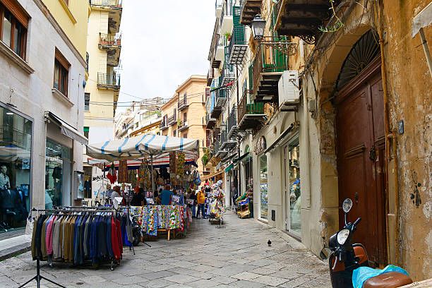 Palermo, Italy - May 16 2025. Bags, jackets and tablecloths on sale at the historic Capo street market in the Monte di Pieta district. Featuring narrow medieval streets, it has a souk-style layout of labyrinthine winding alleys lined with colourful stalls and canopies. Set against the backdrop of weathered historical architecture, Palermo's markets showcase the island's historical position as a cultural crossroads, visible in the goods sold