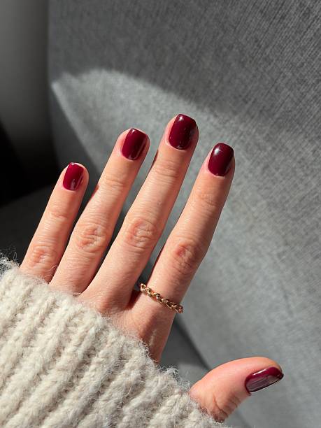 Woman showing her freshly done dark red manicured nails. Autumn manicure design.