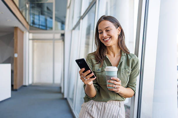 istock Businesswoman standing in office, using mobile phone and drinking coffee 2239165799