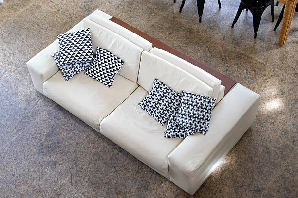 Top view of a white leather sofa with black and white patterned cushions in a modern living room with stone flooring.