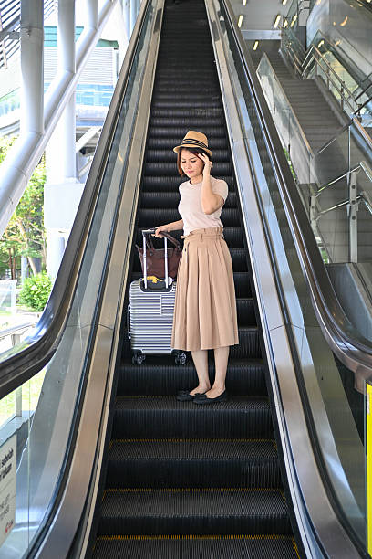 A weary woman on the escalator touches her forehead, struggling with fatigue and headache before boarding.