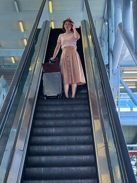 A tired woman on the airport escalator massages her temples, showing signs of stress and discomfort during travel.