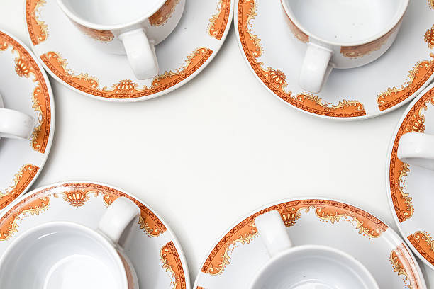 istock Elegant teacups with orange decorative borders arranged on a white surface creating a frame 2239177538