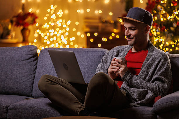 istock Relaxed man on a sofa with laptop and mug during Christmas lights at home 2239186839