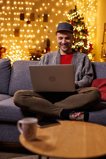 istock Smiling man relaxing on a couch with laptop under festive Christmas lights and tree 2239186843