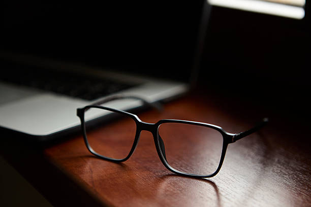 istock Glasses resting on wooden desk beside open laptop 2239195621