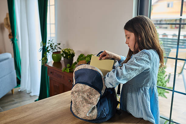 A young girl prepares for school, carefully packing her backpack at home. The scene captures organization, responsibility, and family routine in a bright and cozy interior setting.