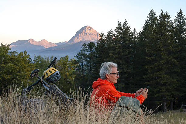 istock Mature man mountain biker uses mobile phone in mountain meadow 2239204739