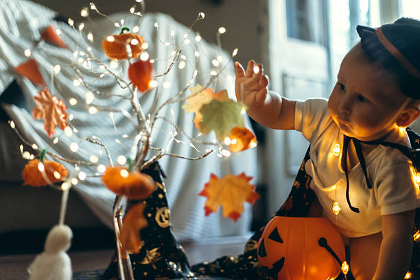 istock A baby dressed in a festive Halloween outfit explores a decorated tree adorned with pumpkins and leaves. The child is captivated by the illuminated ornaments, showcasing a curious expression. 2239220749