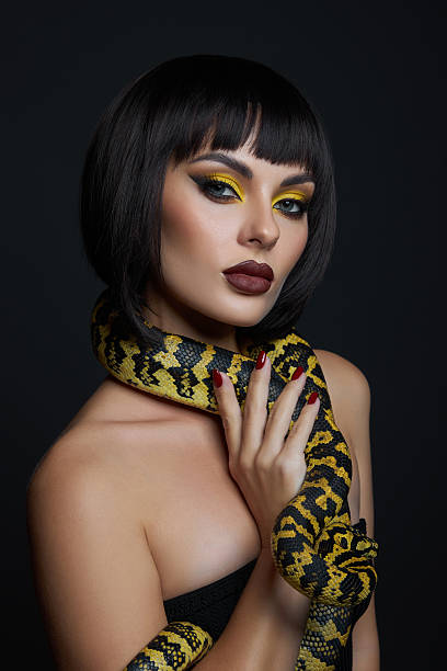istock woman poses confidently with a large snake wrapped around her neck. Her dramatic makeup features bold colors, contrasting with the dark background, creating a striking visual 2239224653