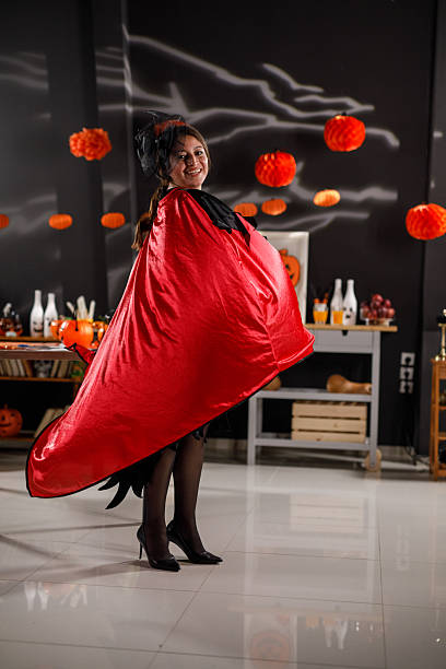 Scary blondy young woman with red devil horns in halloween costume with terrifying make-up trying to catch somebody on yellow background. Halloween celebration, costume party, fear and horror concept.