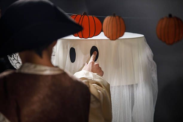 Candid shot of two teenage boys in costumes adding cut out paper eyes and mouth on a lamp to make it spooky for Halloween.