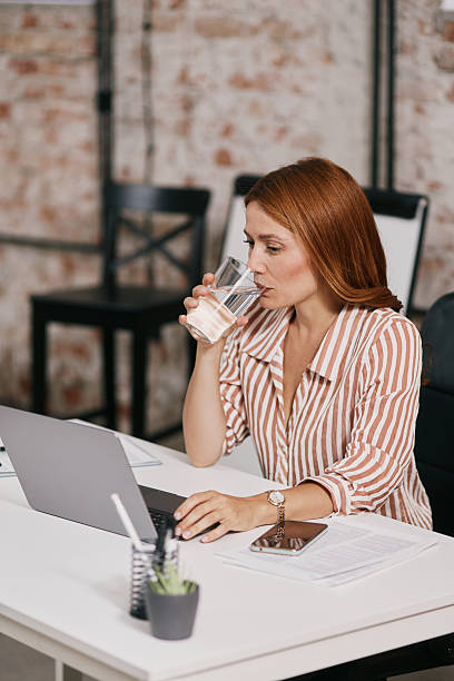 istock Adult Woman Working at White Desk, Drinking Water While Using a Laptop in a Modern Office 2239264253