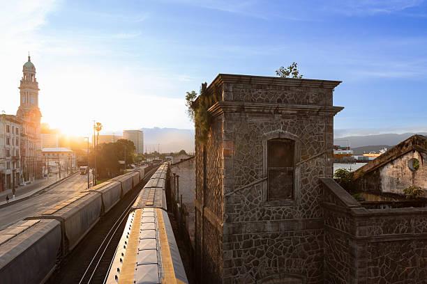 Sunset view of trains and historic architecture near the port of Santos, Brazil. The golden light highlights the stone buildings and the coastal city atmosphere.