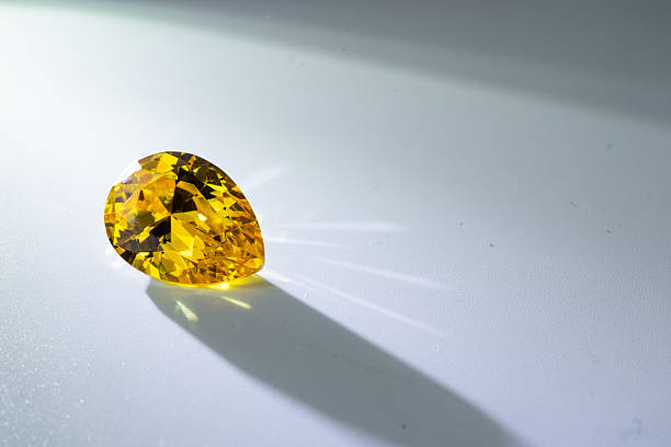 Close up of a brilliant yellow gemstone cut in pear shape, sparkling with radiant reflections on a white background. Perfect for luxury, jewelry, wealth, and elegance design concepts.