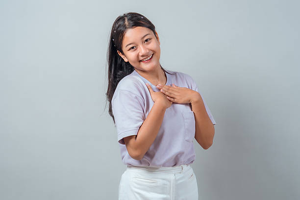 istock Cheerful young Asian woman smiling warmly while touching her chest with both hands, expressing gratitude and sincerity. Studio shot, casual outfit, neutral background. 2239270384