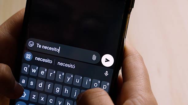istock Close-up of hands holding a smartphone while typing Te necesito! (I Need You!) in a messaging app. 2239279614