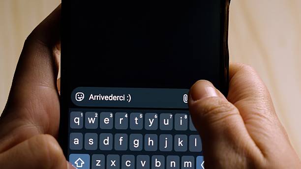 istock Close-up of hands holding a smartphone while typing arrivederci in a messaging app. 2239279631