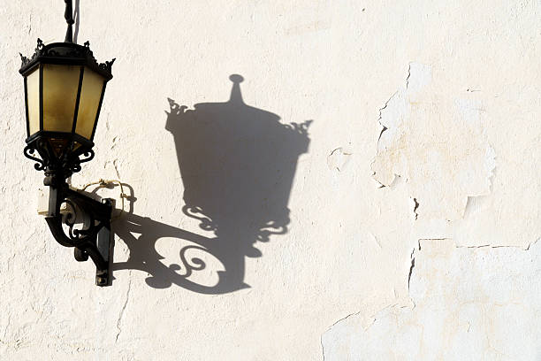 Vintage street lamp creating a prominent shadow on an old peeling wall in sunlight