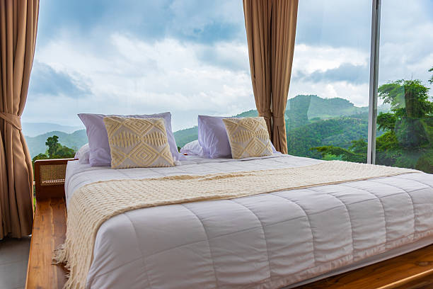 istock Cozy white bed with decorative pillows in a glass room with panoramic mountain view, luxury nature resort concept. 2239300427