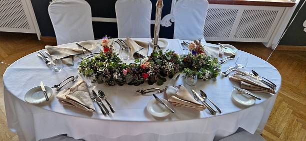 A richly decorated oval dinner table for six people. Elegant dining table set with white linens, glasses, and a floral centerpiece.A very beautiful festive table with candles, plates and glasses.