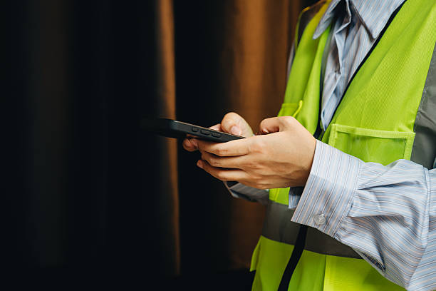 istock Worker in Reflective Safety Vest Using Smartphone in Indoor Setting with Warm Lighting Background 2239307698