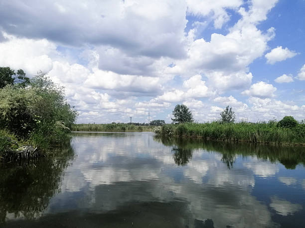 istock Natural landscape includes river, green banks and mirrored clouds. Reflection spreads across water. 2239316858