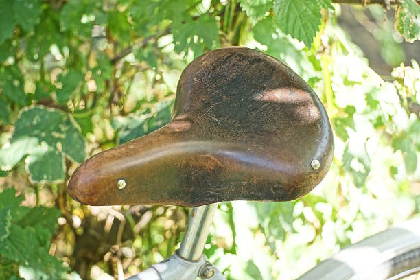 one old brown leather saddle on a  bike among the green vegetation on a summer street