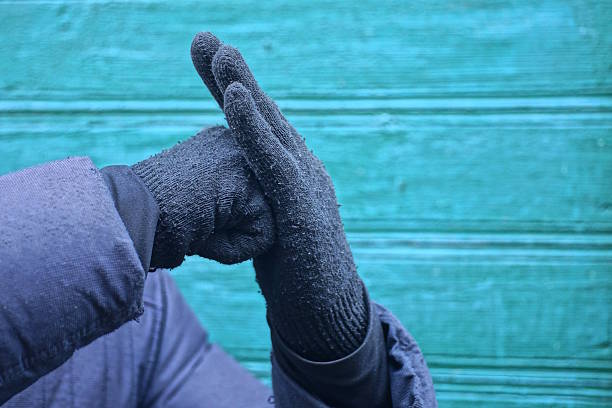 Two hands in black gloves make a signal symbol on a green background on an autumn street