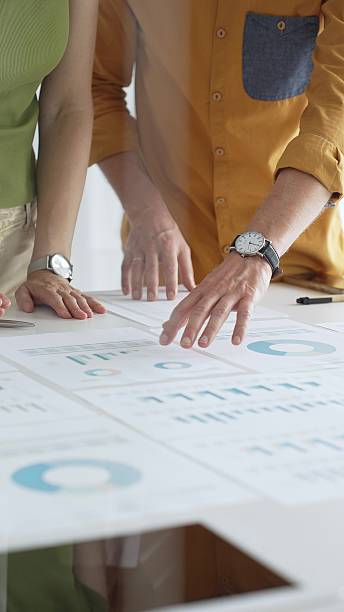 istock Business professionals analyzing financial reports, pointing at data points on charts and graphs lying across white desk surface 2239320252