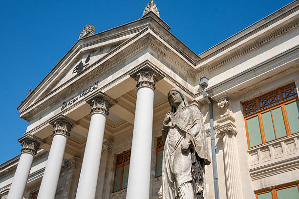 Istanbul, Turkey - 25 August 2025: The Istanbul Archaeological Museum in Turkey features a neoclassical façade with prominent columns and a triangular pediment. A classical statue stands in front, showcasing detailed drapery in the sculpture. The building's exterior includes ornate window frames and decorative elements, typical of classical architectural style. The structure is bathed in sunlight against a clear blue sky, highlighting its historical grandeur