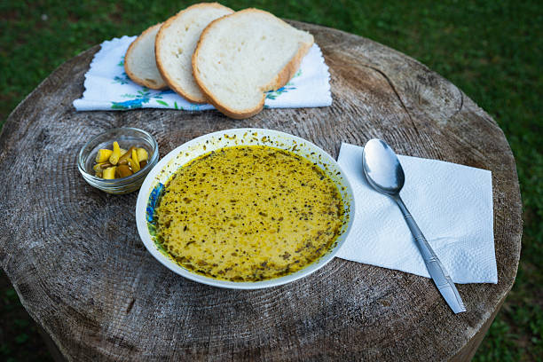 Porcini mushroom soup served outdoors with sliced bread and pickled chili peppers on a rustic tree stump table in Apuseni Mountains, Romania