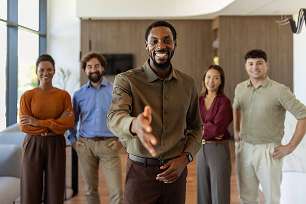 istock Welcoming Corporate Team: Black Man Extending Hand with Colleagues in Background 2239324724