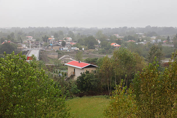 A view of the village among green trees and rainy weather.