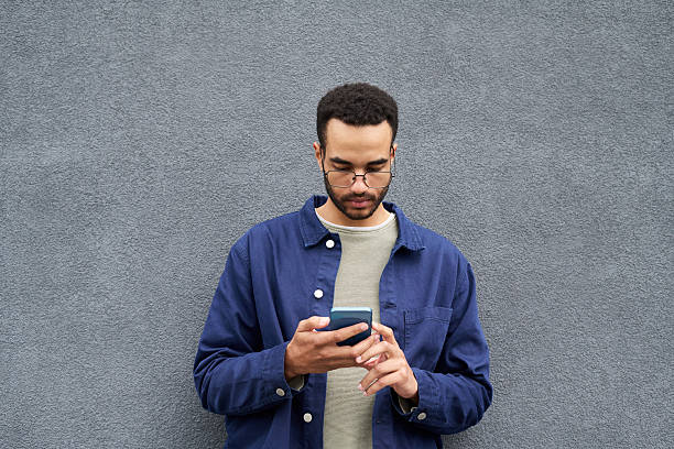 istock Young Black Man Browsing Smartphone While Standing Against Concrete Wall 2239331656