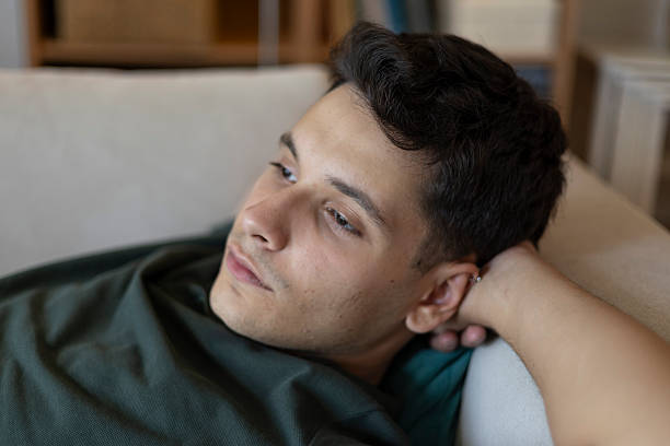 istock Young man relaxing on a couch at home, deep in thought, looking away 2239333921