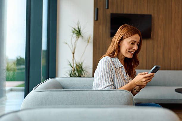 istock Woman smiling and texting on cell phone at home 2239334740